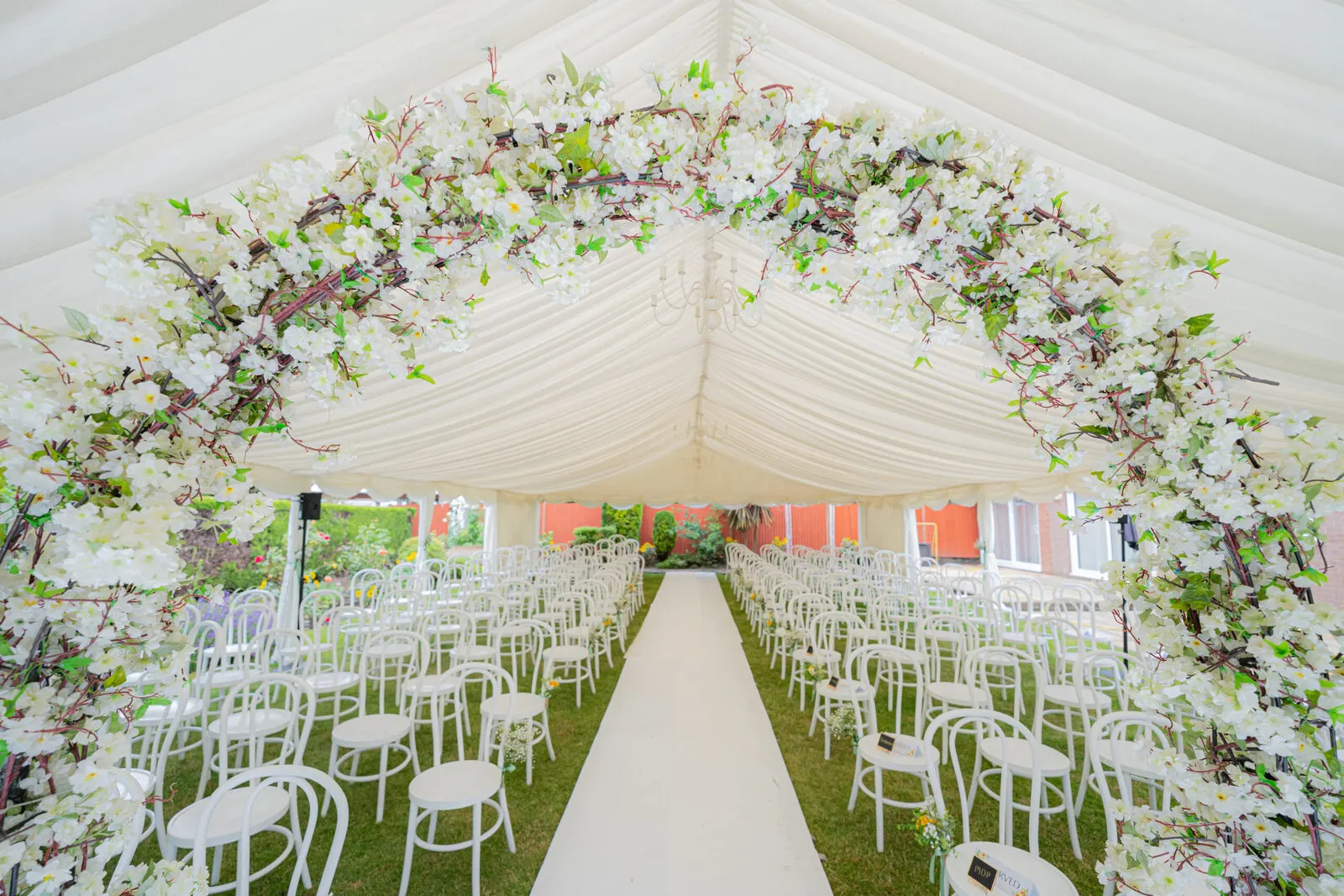 Wedding ceremony aisle under a lined marquee with floral arch